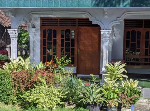 Aménagement paysager d'une entrée de maison avec un parterre sans entretien. On y voit des plantes vivaces d'ombre (Heuchères pourpres et Hostas verts), un paillage minéral de graviers et des bordures nettes le long d'une allée.