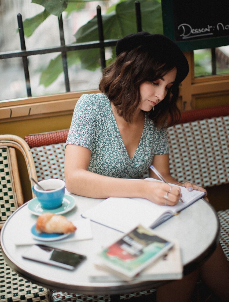 Young woman writing notes in a cozy café with a cup of coffee and a croissant.