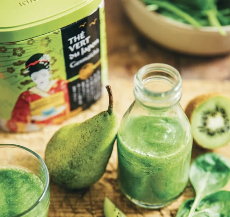 Boîte en métal vert de thé vert du Japon à côté d'une bouteille en verre de smoothie vert bien-être, d'une poire et de feuilles d'épinards frais.